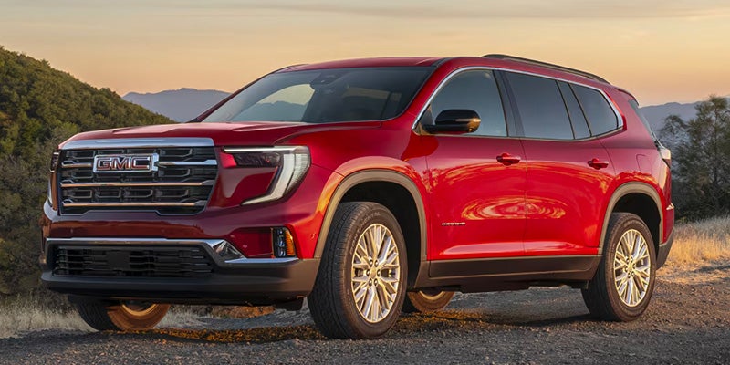 A red Acadia Parked near hills on ground