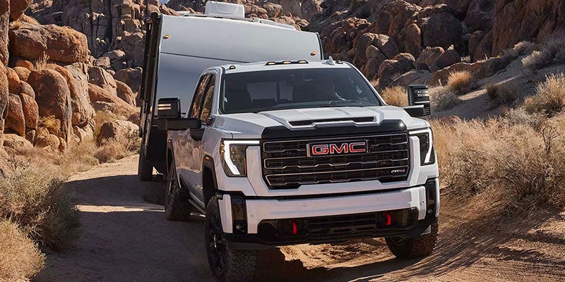 A white Sierra towing a container in hills area
